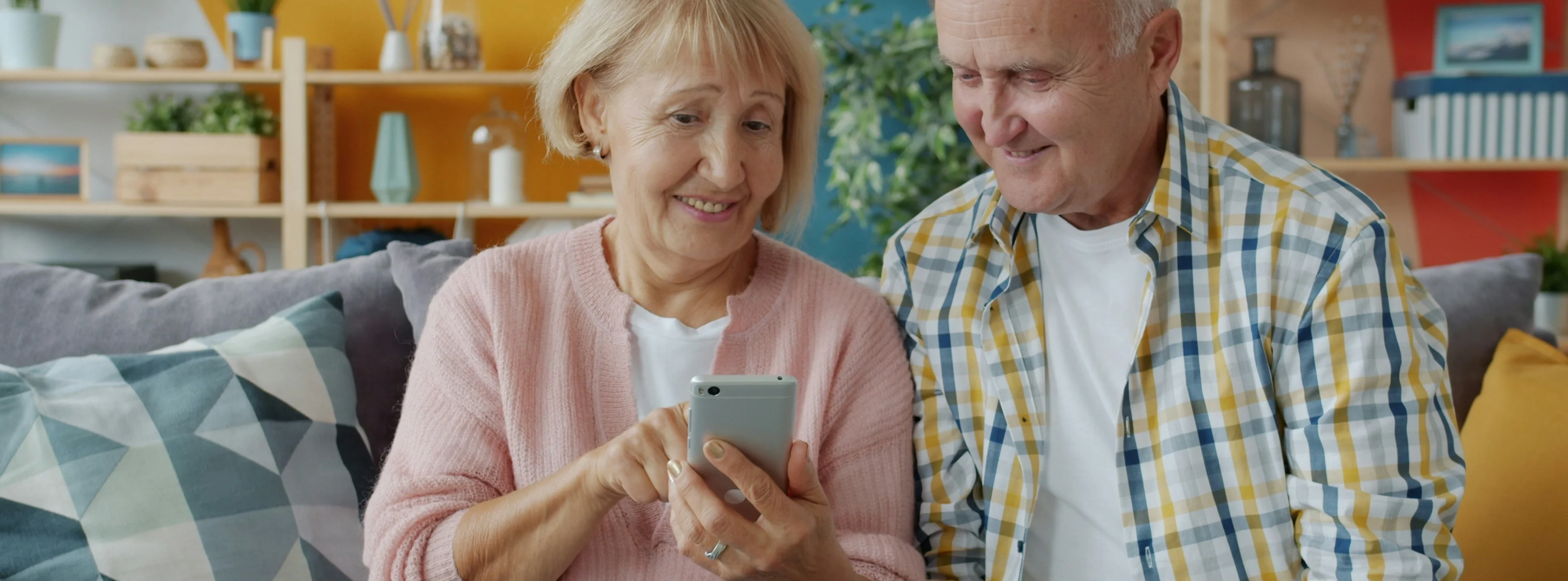 Eine ältere Frau sitzt mit ihrem Ehemann auf dem Sofa in einer modernen Wohnung und benutzt ein Smartphone, indem sie den Bildschirm berührt
