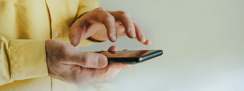 Eine Person hält ein Smartphone in der Hand und tippt darauf.
